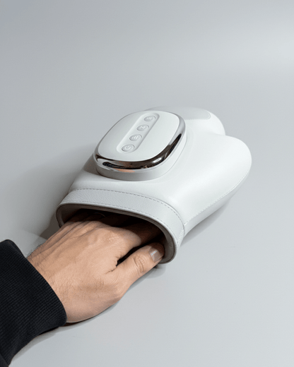 Personne utilisant un handrelax électrique sur sa main gauche, avec un sourire détendu. L'appareil enveloppe les doigts et la paume pour un massage profond des muscles et articulations